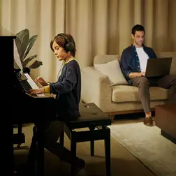 Yamaha-Piano Ein kleiner Junge spielt Klavier während sein Vater auf dem Sofa zuhört.